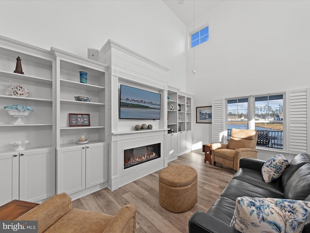 living room with a glass covered fireplace, light wood finished floors, and high vaulted ceiling