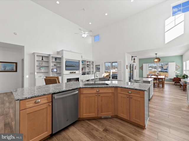 kitchen featuring light wood finished floors, a warm lit fireplace, a sink, dishwasher, and open floor plan