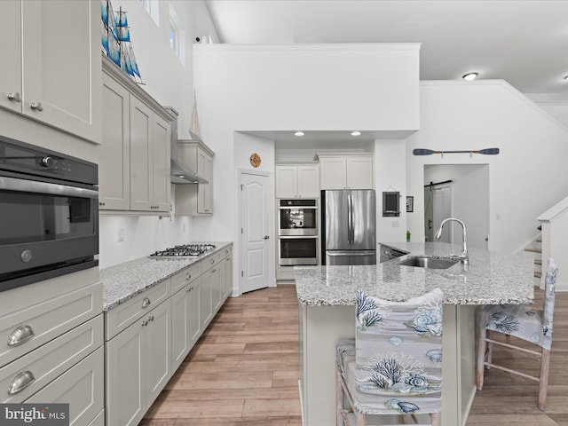 kitchen with light wood-type flooring, a barn door, light stone counters, stainless steel appliances, and a sink