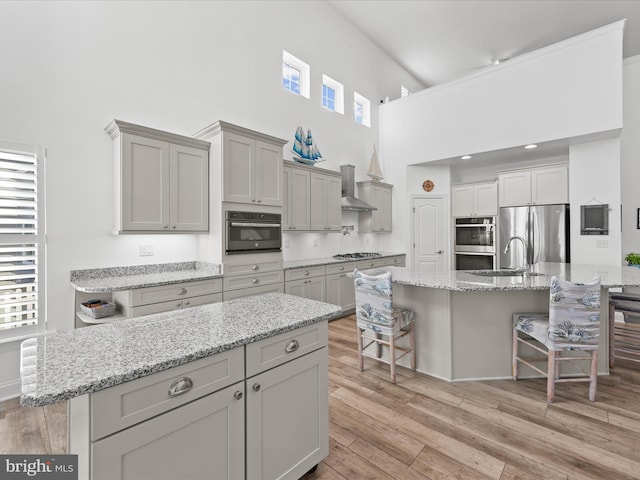 kitchen with a center island with sink, a breakfast bar area, light wood-type flooring, stainless steel appliances, and wall chimney exhaust hood