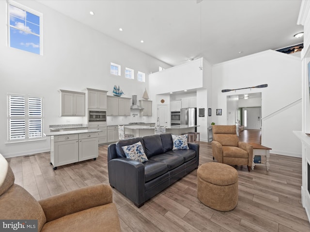 living area featuring recessed lighting, baseboards, light wood-style floors, and a towering ceiling