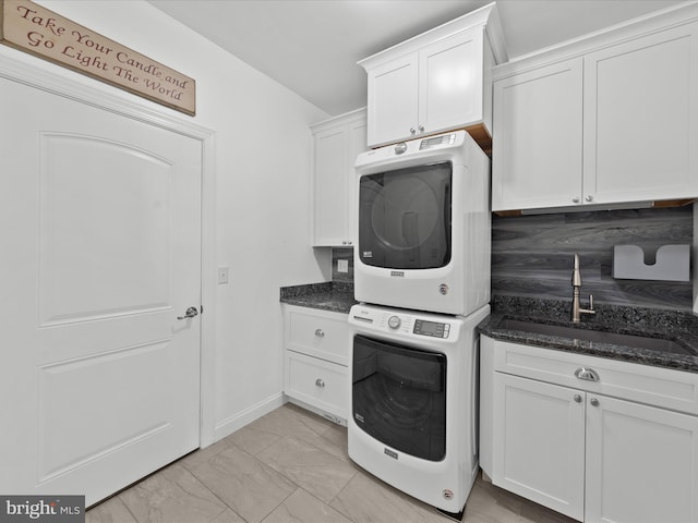 laundry room featuring baseboards, cabinet space, a sink, stacked washer and dryer, and marble finish floor