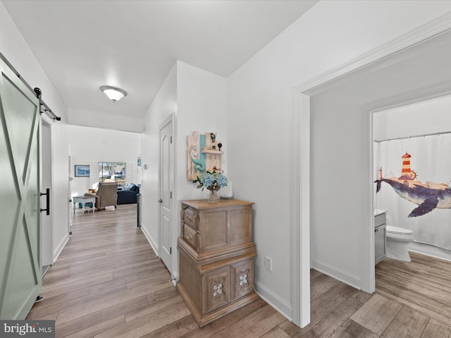 hallway featuring a barn door, baseboards, and light wood finished floors