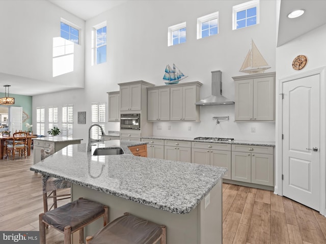 kitchen featuring gray cabinets, a sink, a kitchen breakfast bar, appliances with stainless steel finishes, and wall chimney exhaust hood