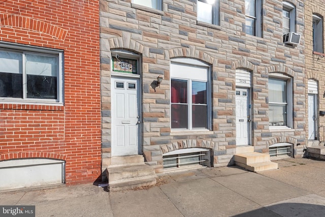 doorway to property featuring stone siding, brick siding, and cooling unit