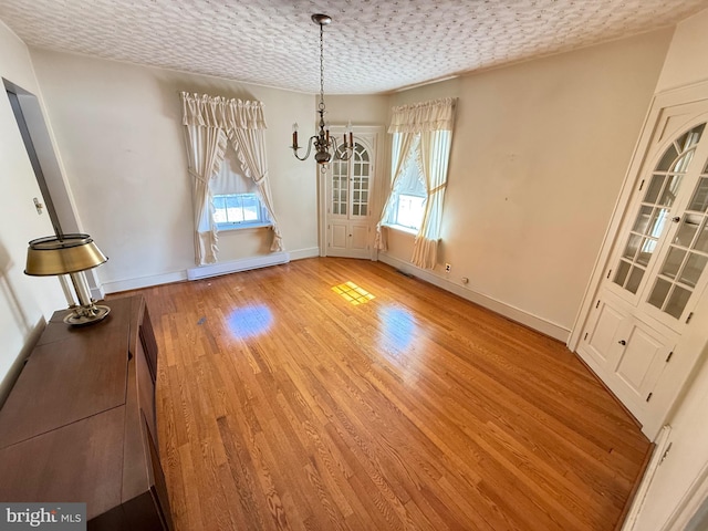 unfurnished dining area featuring light wood-style flooring, a textured ceiling, a baseboard heating unit, and baseboards