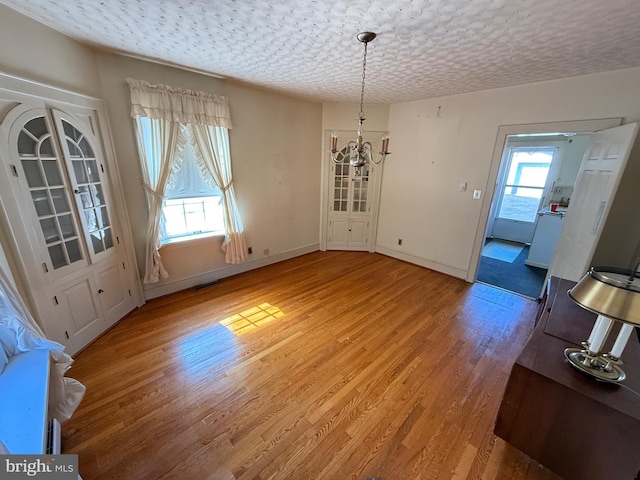 unfurnished dining area featuring light wood-type flooring, plenty of natural light, a chandelier, and a textured ceiling