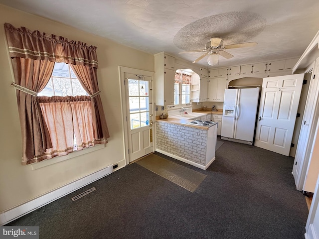 kitchen featuring a peninsula, plenty of natural light, a baseboard radiator, and white fridge with ice dispenser