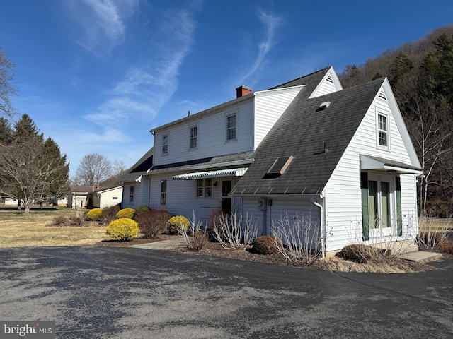 view of front facade featuring a garage, a shingled roof, and a chimney