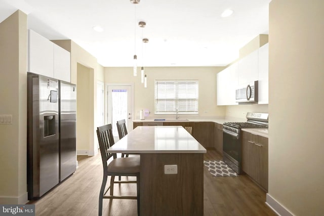 kitchen with wood finished floors, light countertops, white cabinets, appliances with stainless steel finishes, and a kitchen bar