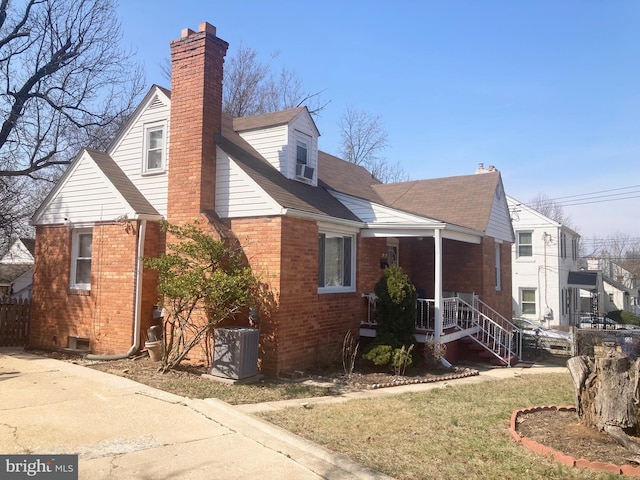 view of property exterior featuring a porch, cooling unit, brick siding, a yard, and a chimney