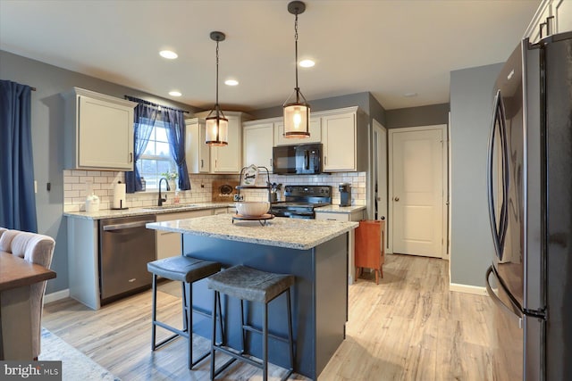 kitchen with black appliances, light wood finished floors, a sink, and a center island