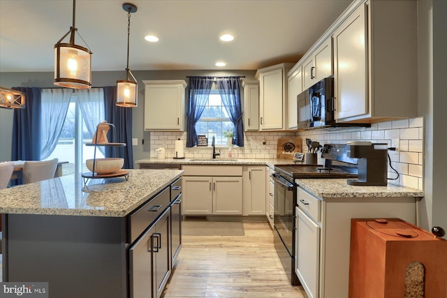 kitchen with pendant lighting, backsplash, light wood-style floors, a sink, and black appliances