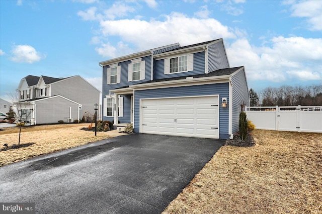 traditional home featuring aphalt driveway, an attached garage, fence, and a gate