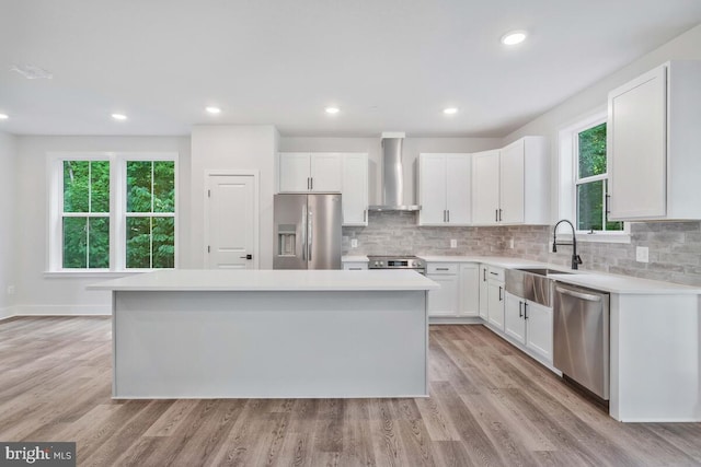 kitchen featuring white cabinets, a kitchen island, stainless steel appliances, wall chimney range hood, and a sink