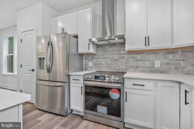 kitchen with light countertops, appliances with stainless steel finishes, light wood-type flooring, backsplash, and wall chimney exhaust hood