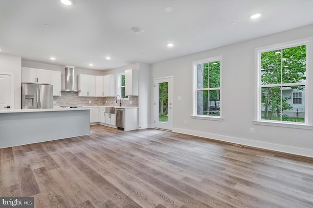 kitchen with tasteful backsplash, light wood-style flooring, appliances with stainless steel finishes, light countertops, and wall chimney range hood