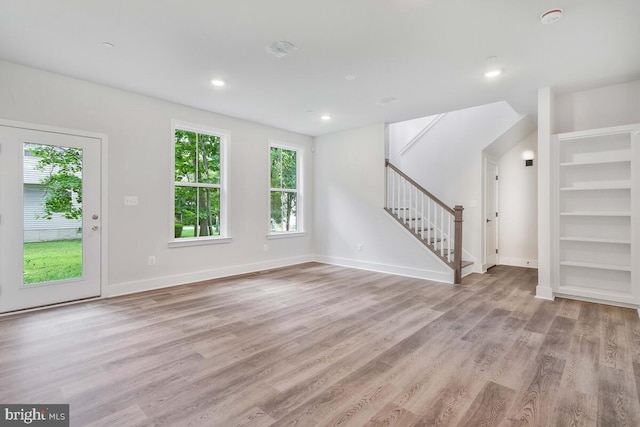 unfurnished living room featuring light wood finished floors, stairs, baseboards, and recessed lighting