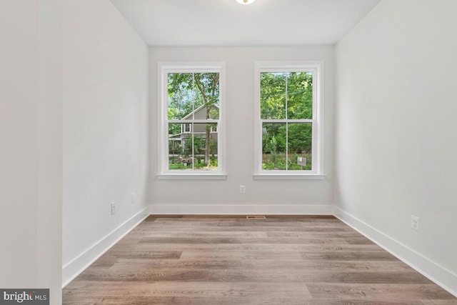 unfurnished room featuring baseboards, a wealth of natural light, and wood finished floors