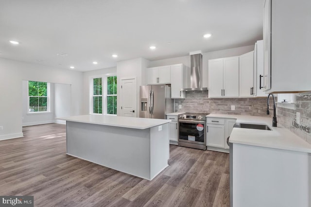 kitchen featuring light wood-style flooring, stainless steel appliances, a sink, wall chimney exhaust hood, and tasteful backsplash