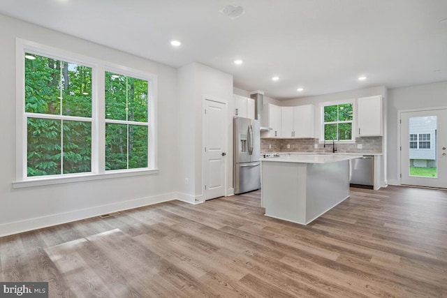 kitchen featuring stainless steel appliances, white cabinetry, light countertops, backsplash, and light wood finished floors