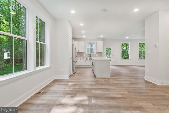 kitchen featuring light wood finished floors, tasteful backsplash, a kitchen island, freestanding refrigerator, and white cabinetry