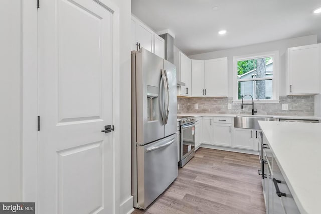 kitchen featuring white cabinets, light wood-style flooring, appliances with stainless steel finishes, light countertops, and a sink