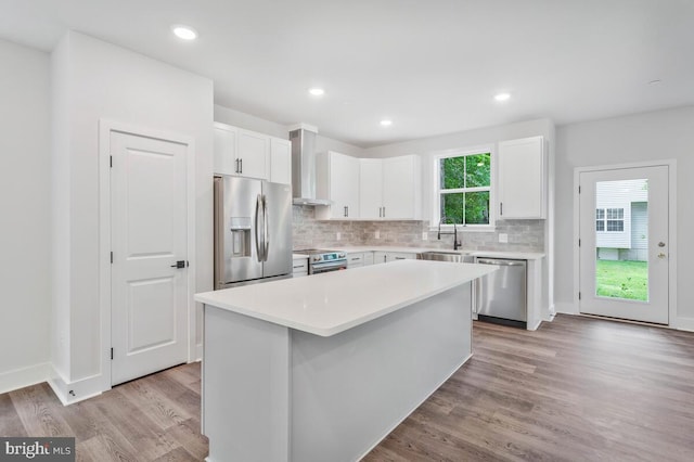 kitchen with stainless steel appliances, light wood-style flooring, white cabinetry, a sink, and wall chimney range hood