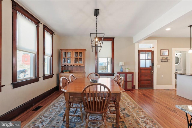 dining room featuring a wealth of natural light, stacked washer and clothes dryer, baseboards, and wood finished floors