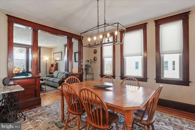 dining room featuring ornate columns, a textured ceiling, baseboards, and hardwood / wood-style floors