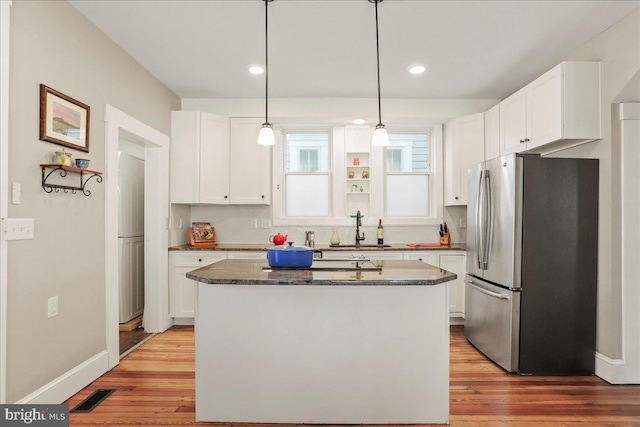 kitchen featuring a sink, visible vents, white cabinets, light wood-type flooring, and freestanding refrigerator