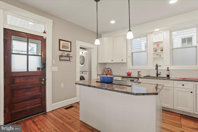 kitchen with a kitchen island, white cabinets, a sink, and stacked washing maching and dryer