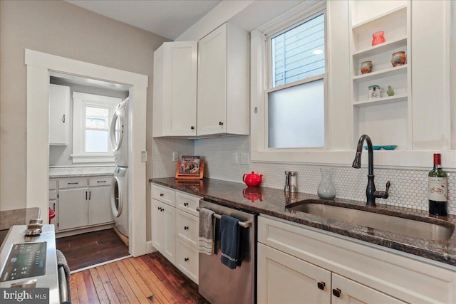 kitchen with dark stone countertops, stacked washer / dryer, dishwasher, and a sink