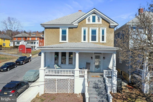 view of front facade with a porch, a shingled roof, and stucco siding