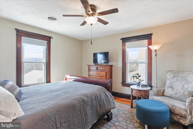 bedroom featuring a ceiling fan, a textured ceiling, visible vents, and wood finished floors