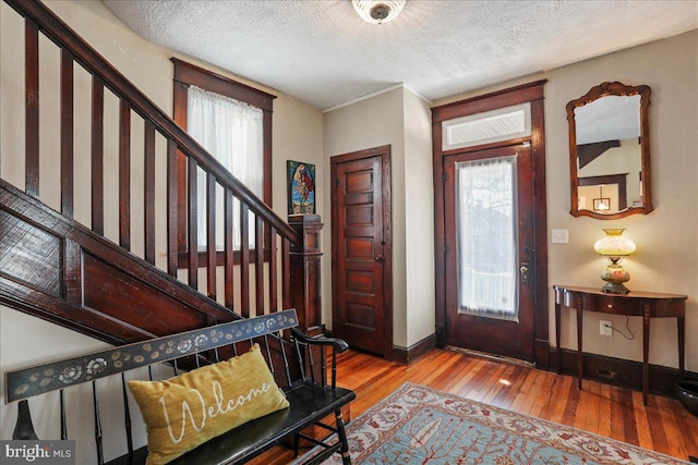 entrance foyer with wood-type flooring, stairs, baseboards, and a textured ceiling