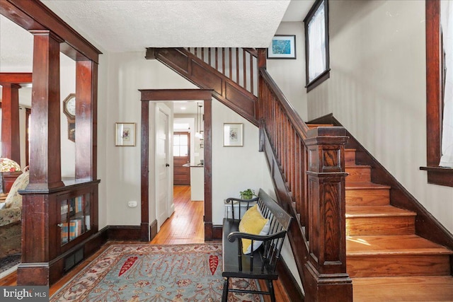 stairway with ornate columns, a textured ceiling, baseboards, and hardwood / wood-style flooring