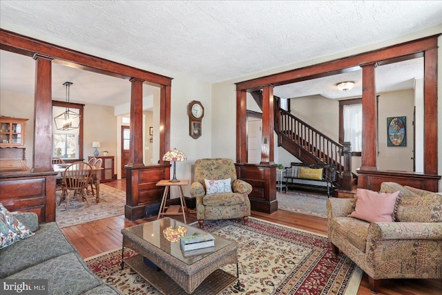 living room with a textured ceiling, stairway, ornate columns, and wood finished floors