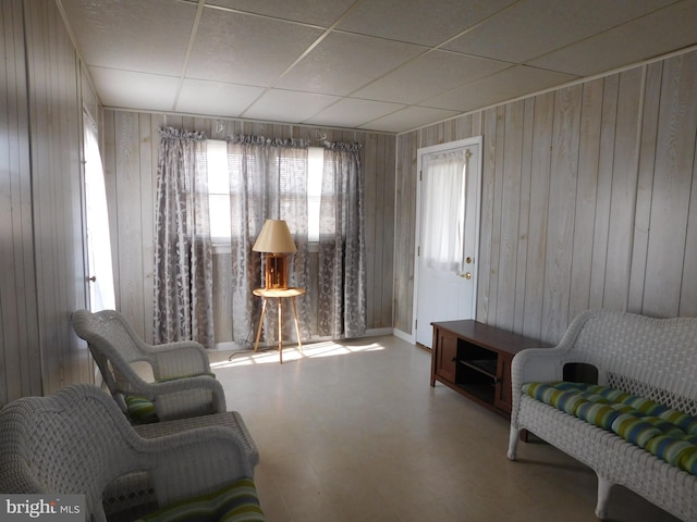 sitting room featuring wooden walls, a drop ceiling, and tile patterned floors