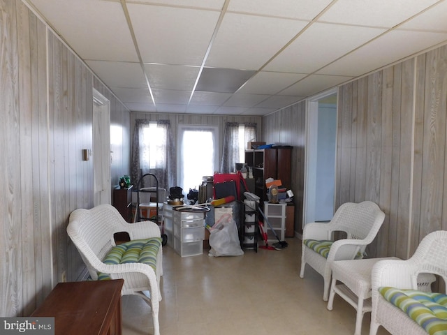 sitting room with tile patterned floors, a paneled ceiling, and wooden walls