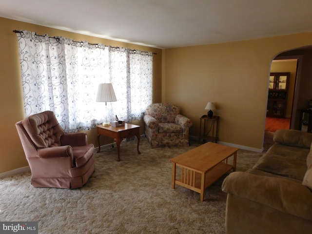 carpeted living area featuring arched walkways and baseboards