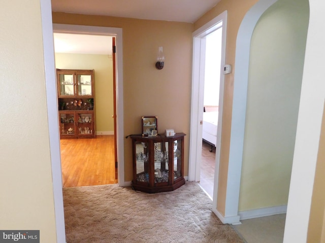 hallway with carpet floors, arched walkways, and baseboards