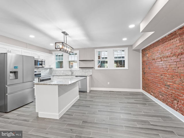 kitchen with light stone counters, brick wall, a sink, white cabinetry, and appliances with stainless steel finishes