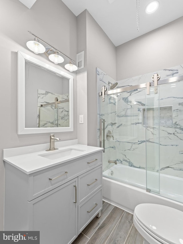 bathroom with visible vents, toilet, combined bath / shower with glass door, vanity, and wood finished floors