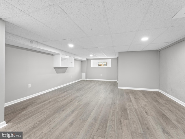 below grade area with recessed lighting, wood finished floors, a paneled ceiling, and baseboards