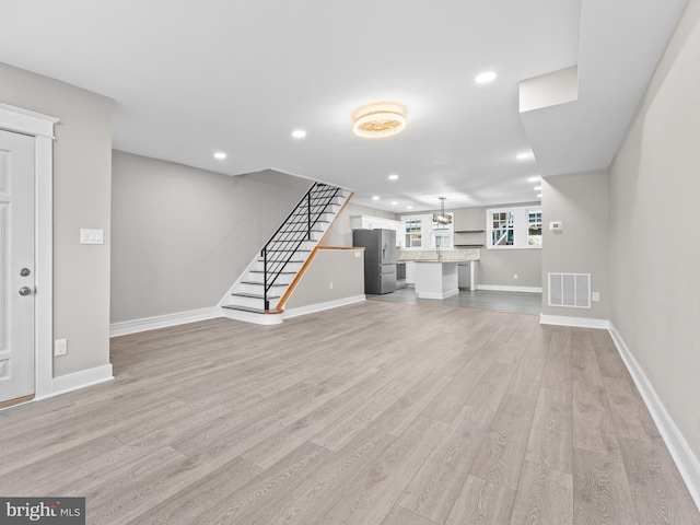 unfurnished living room with light wood-style flooring, recessed lighting, visible vents, baseboards, and stairs