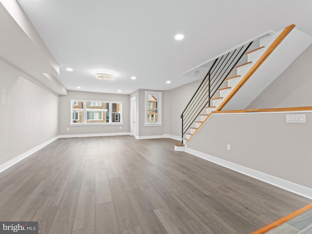 unfurnished living room featuring baseboards, stairway, wood finished floors, and recessed lighting