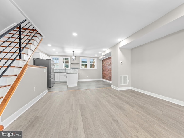 unfurnished living room with recessed lighting, visible vents, baseboards, stairway, and light wood finished floors