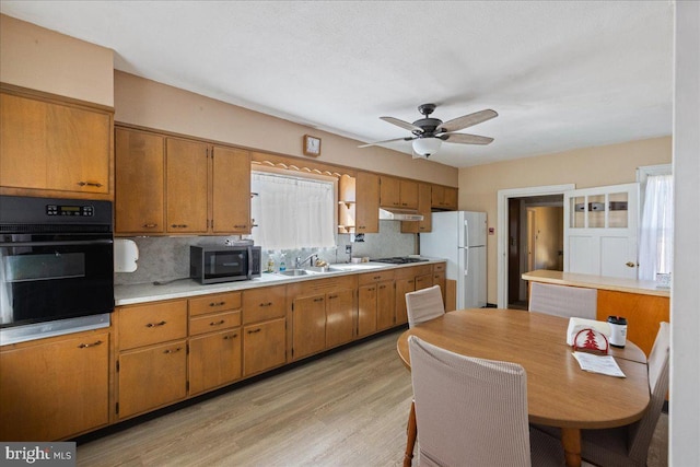 kitchen featuring ceiling fan, brown cabinets, under cabinet range hood, light countertops, and black appliances