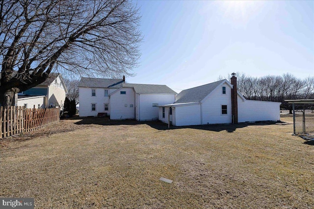 rear view of property with a lawn, a chimney, and fence